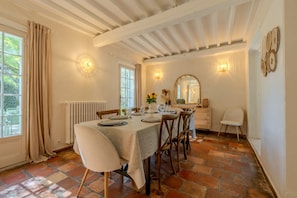 A dining room with a table set for four, a radiator, a window with curtains, and a mirror on the wall.