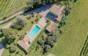 An aerial view of a property with a swimming pool, a patio area, and a house with a tiled roof.