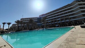 A swimming pool with a clear blue sky and a multi-story building in the background. - Tolip Resort El Galala Heights (Ataqah)