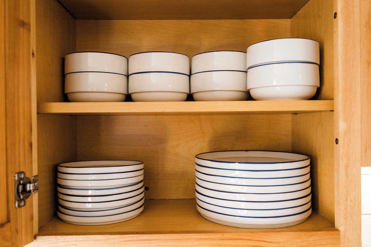 A wooden cabinet with two shelves, each holding stacks of white plates with blue stripes.