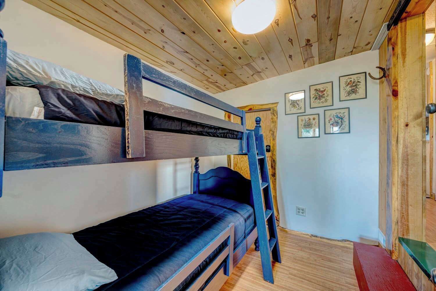 A bunk bed room with a wooden ceiling and a ladder.