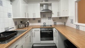 Eine kleine Küche mit weißen Schränken, einem schwarzen Fliesenboden, einer Holz Arbeitsplatte und einem eingebauten Backofen.