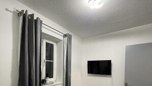 Ein Schlafzimmer mit einem Bett, einem Fenster mit Vorhängen, einem an der Wand montierten Flachbildfernseher und einer Tür.