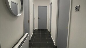 Ein schmaler Korridor mit dunklen Fliesen, weißen Wänden und Türen an beiden Seiten.