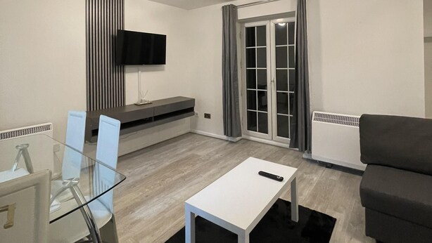 Ein modernes Wohnzimmer mit Glastisch, Sofa und Wandfernseher.