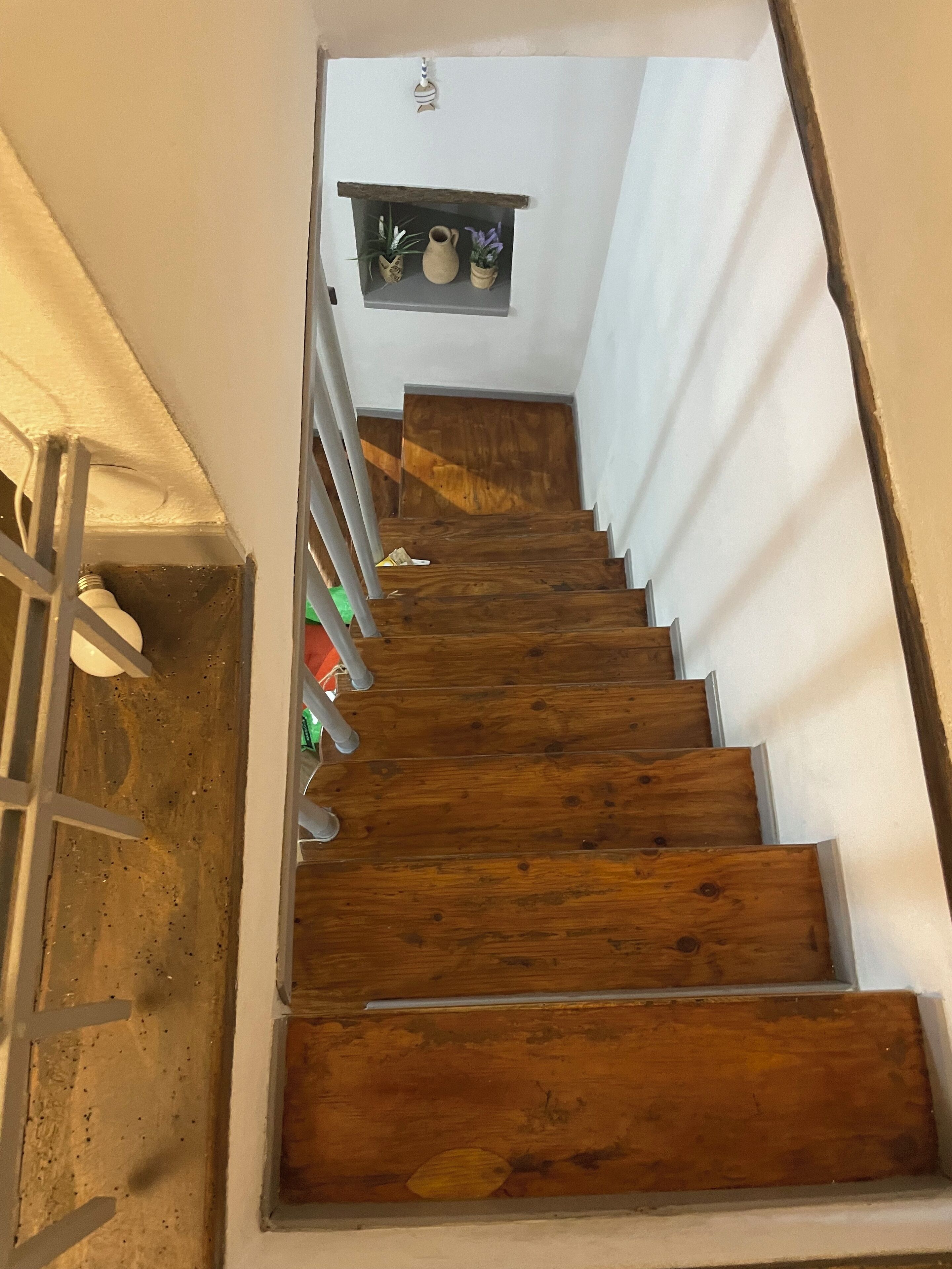 A wooden staircase with a white wall and a shelf with decorative items.