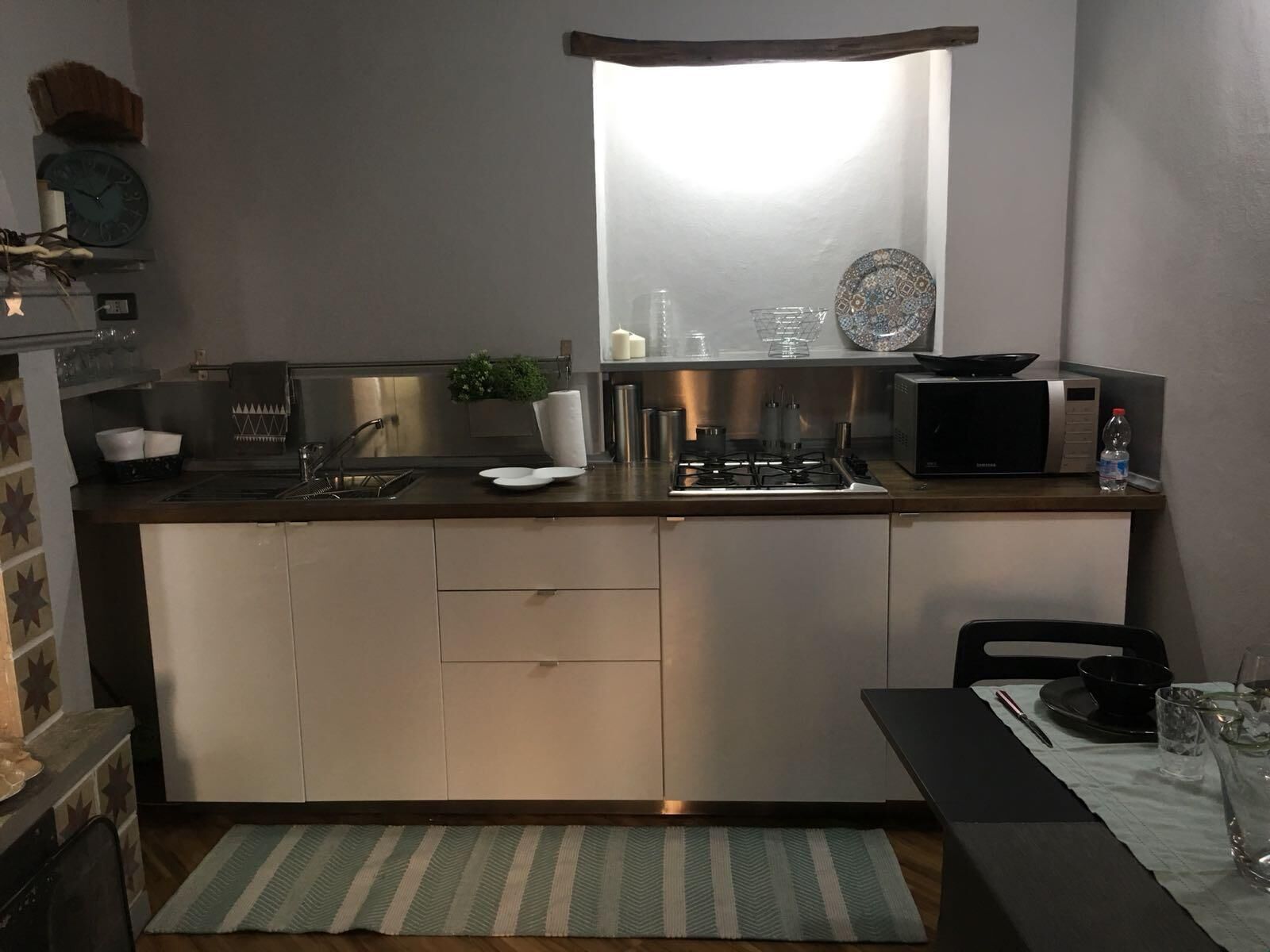 Una cocina compacta con microondas integrado, un lavamanos y una pequeña ventana sobre la encimera.