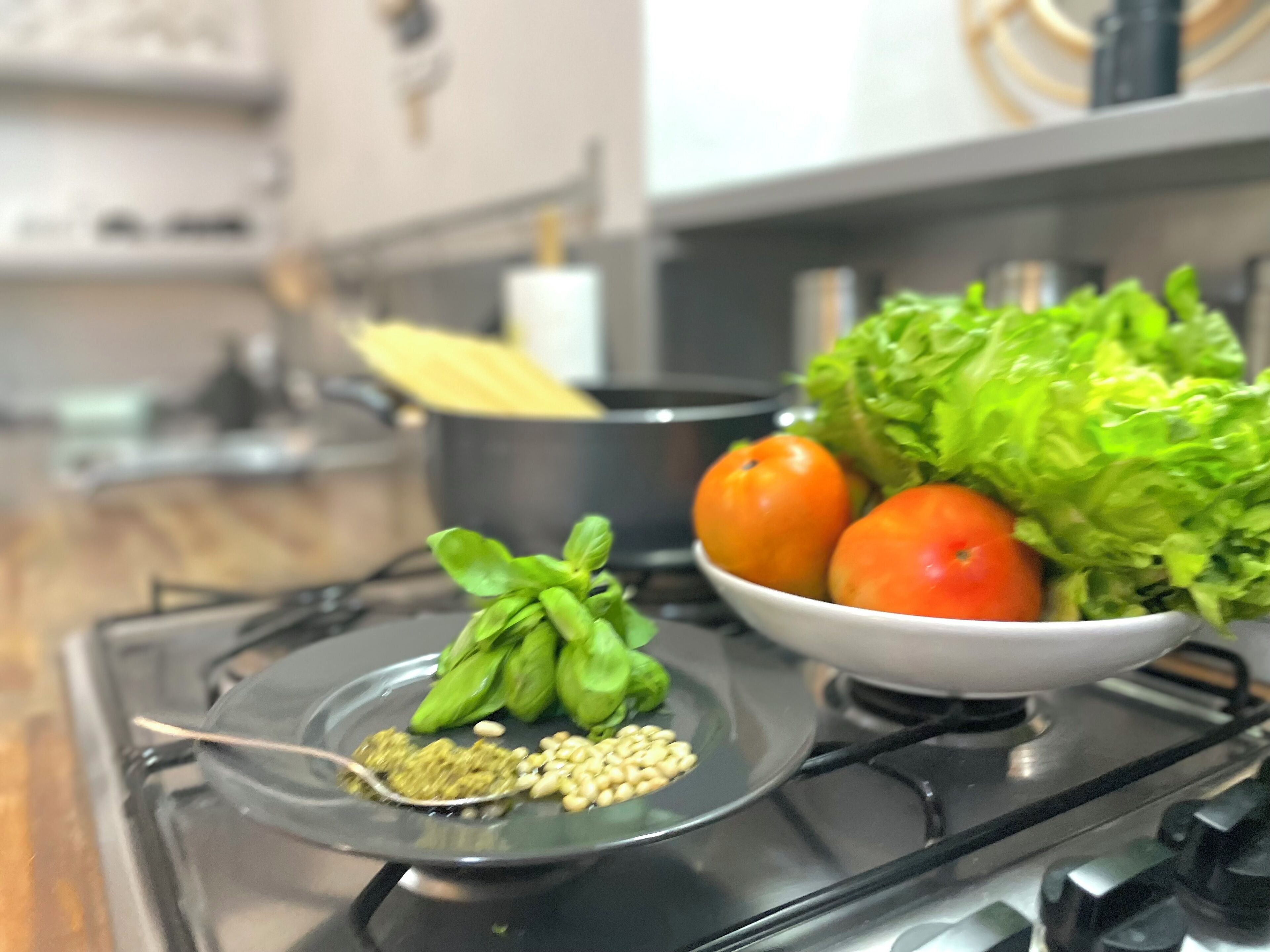 Una estufa de cocina con un bol de tomates, lechuga y albahaca encima.