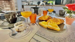 Una escena de desayuno con croissants, jugo de naranja, café y té sobre una mesa.