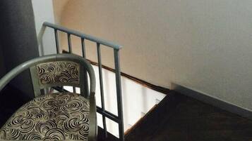 Una escalera con una silla al pie, un estante con adornos, y una pared blanca.