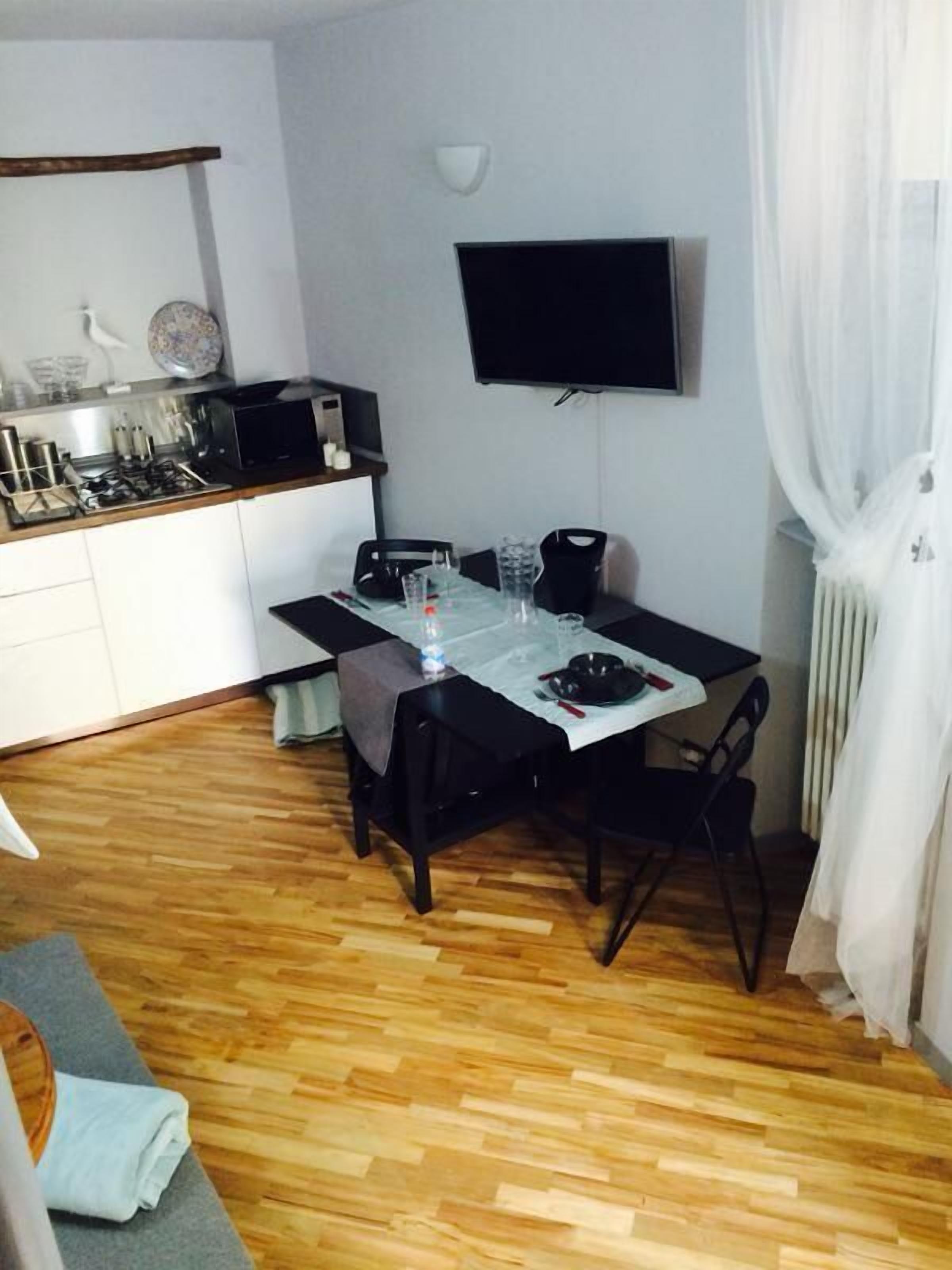 A compact living space with a kitchenette, a dining table, and a flat-screen TV mounted on the wall.