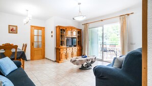 Een woonkamer met een bank, een salontafel, een televisie en een kast. Een deur leidt naar een balkon.