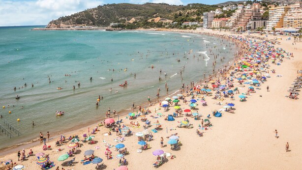 Een druk strand met veel parasols en mensen die van het water genieten.