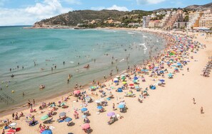 Una playa concurrida con numerosos sombrillas y gente disfrutando del agua.