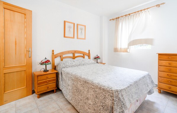 Un dormitorio con una cama de madera, dos mesitas de noche con lámparas, un aparador de madera y una ventana con cortinas.