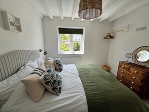 A bedroom with a bed, dresser, window, and a hanging light fixture. - Beautiful cottage Snugglers Nook in heart of Bude near the beach, river & canal. (Bude)