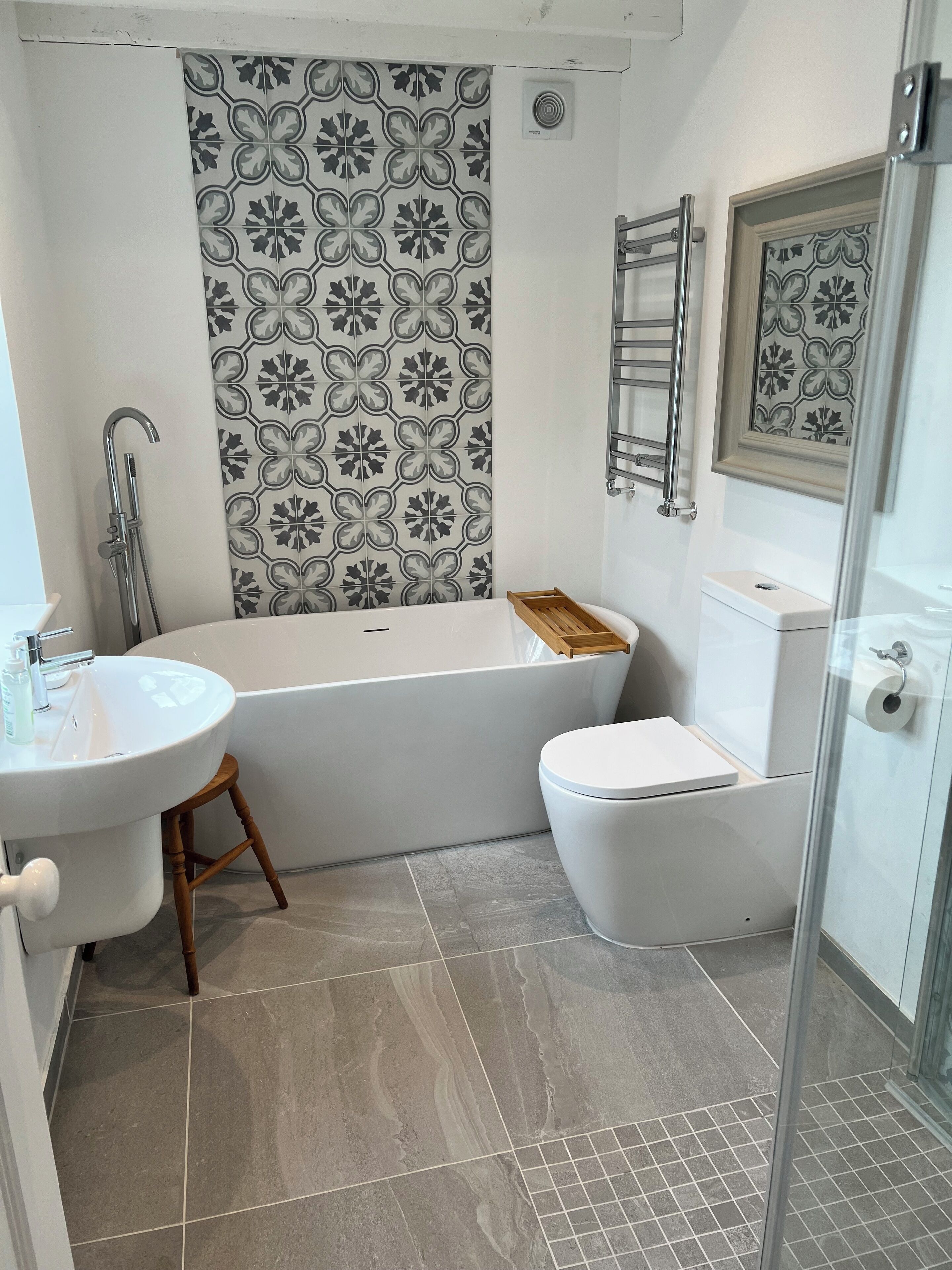 A bathroom with a white bathtub, a white toilet, a wooden stool, a sink, and a shower area.
