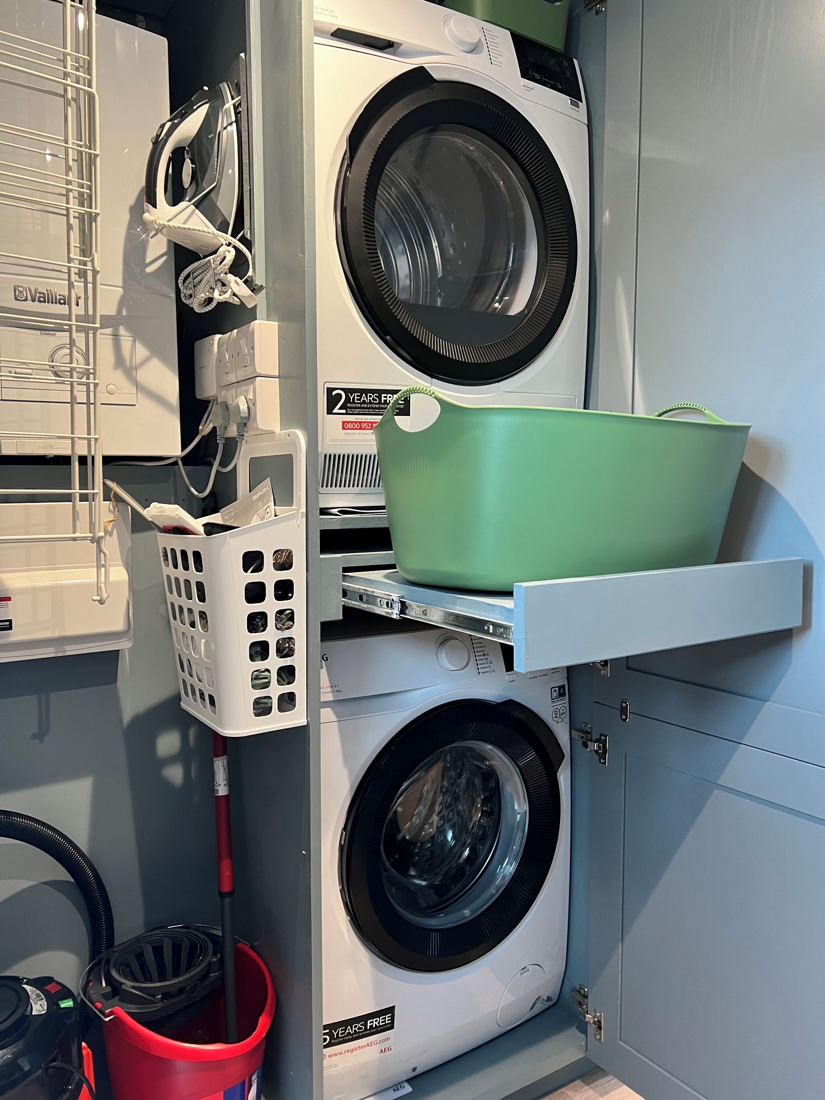 Een wasserij met gestapelde wasmachines en drogers, een droogrek en een mand.