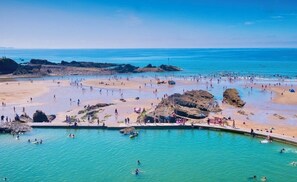 A coastal beach with clear blue waters, rocky formations, and a sandy shore.