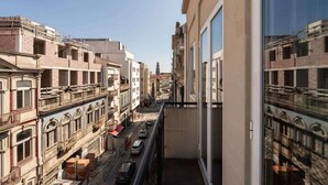 Une rue étroite en milieu urbain, bordée d’immeubles à plusieurs étages, avec un ciel dégagé et le clocher d’une église visible au loin.