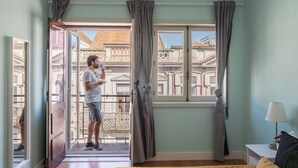 Une chambre avec un balcon, un lit, une table de chevet et une fenêtre avec des rideaux.