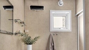 Ein Badezimmer mit einem weißen Waschbecken, einem Spiegel und einer Toilette. Am Waschbecken befinden sich ein Handtuchhalter und ein Blumentopf.