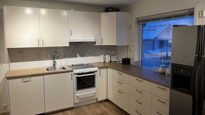 Eine moderne Küche mit weißen Schränken, einem Backofen, einem Spülbecken und einem Fenster mit Blick auf ein Haus.