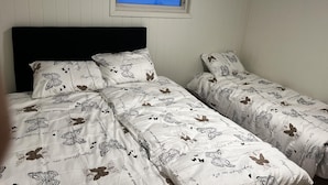Ein Schlafzimmer mit zwei Betten, beide mit weißer Bettwäsche mit Schmetterlingsmustern und Text. Über den Betten befindet sich ein Fenster mit Blick auf eine verschneite Landschaft.