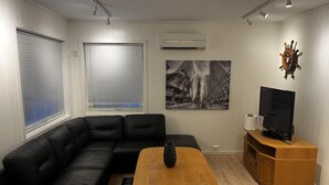 Ein Wohnzimmer mit schwarzem Ledersofa, einem Holztisch, einem Fernseher auf einem Holzständer und einem großen Stadtbild an der Wand.