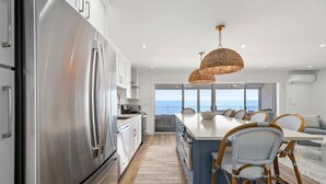 A modern kitchen with stainless steel appliances, a central island with seating, and a view to the sea. - Coastal Inspired Three Bedroom Oceanfront Condo (Ocean City)
