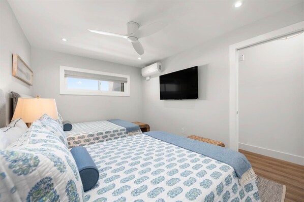 A bedroom with two beds, a ceiling fan, a TV, and a window.