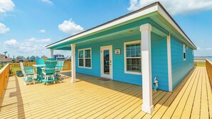 A blue house with a wooden deck and turquoise chairs.