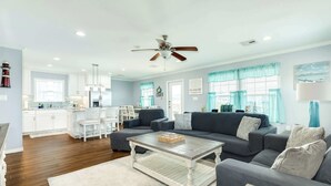 A spacious living area with a large gray sectional sofa, a wooden coffee table, and a kitchen in the background.