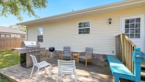 Un jardin avec un barbecue, des chaises et une terrasse en bois.