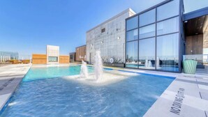 A swimming pool with a water fountain, surrounded by modern buildings with large windows. - Luxury Oasis - Rooftop pool & Rainey St access (Austin)