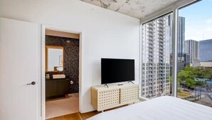 A modern bedroom with a large bed, a television on a cabinet, and a bathroom with a mirror and sink. - Luxury Oasis - Rooftop pool & Rainey St access (Austin)