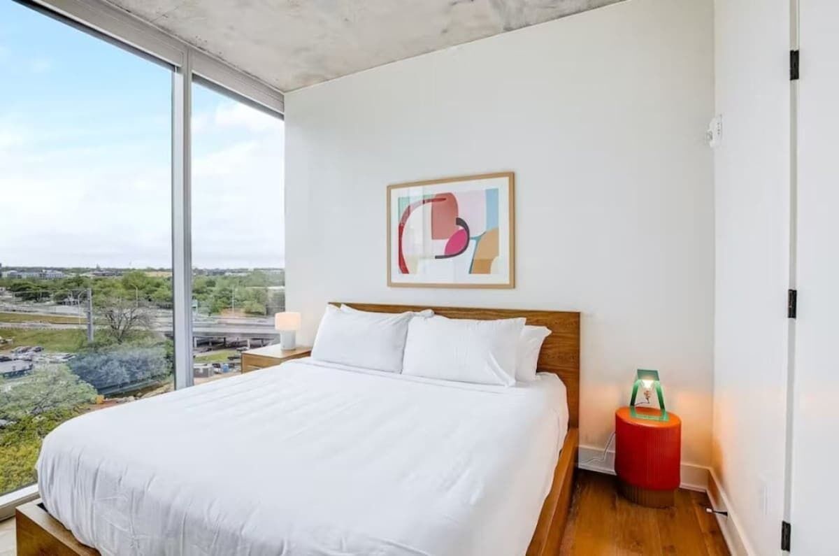 Una habitación de hotel moderna con una cama grande, vistas de la ciudad y una obra de arte abstracta en la pared.