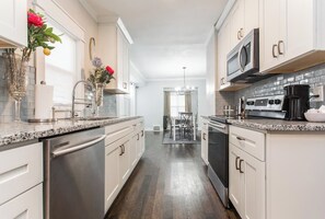 A modern kitchen with white cabinetry, granite countertops, a stainless steel dishwasher, a double oven, and a black range hood. - CityRetreat: Fenced Yard, Free Parking (Kansas City)