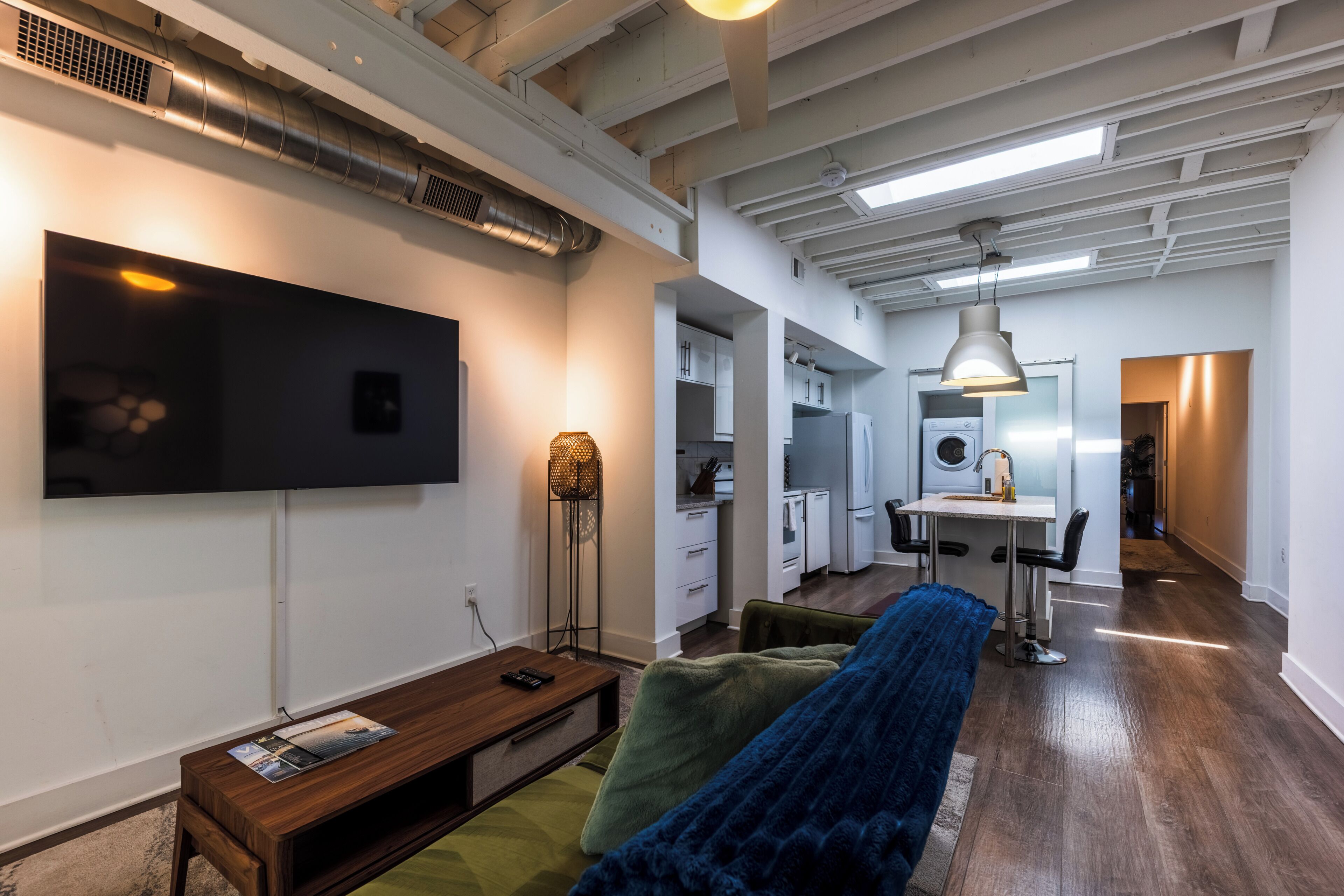 A modern living room with a flat-screen TV, a sofa, and a dining area with a table and chairs.