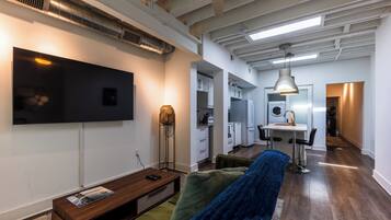 A modern living room with a flat-screen TV, a sofa, and a dining area with a table and chairs.