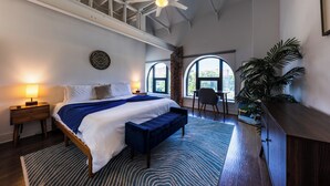 A bedroom with a bed, bedside lamps, a bench, a desk, and a large window. - Charming Space with Parking/King Bed/Street Car (Kansas City)
