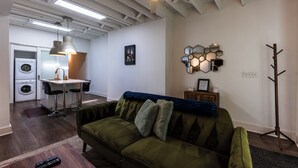A modern living room with a green sofa, a coffee table, a wall-mounted hexagonal mirror, and a coat rack. - Charming Space with Parking/King Bed/Street Car (Kansas City)