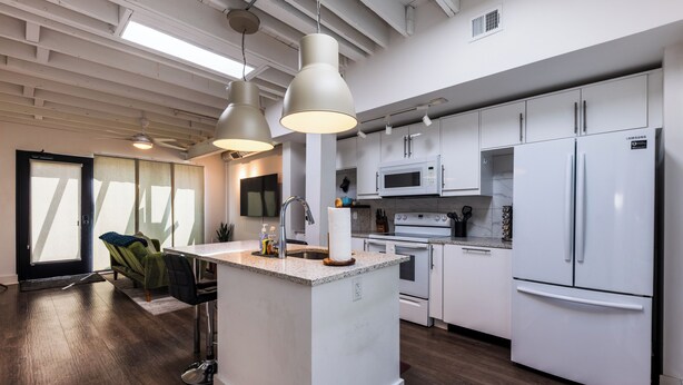 A modern kitchen with white appliances, a central island, and a dining area with a sofa and chairs. - Charming Space with Parking/King Bed/Street Car (Kansas City)