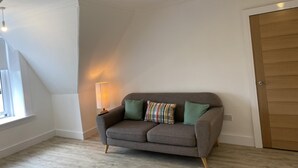Ein Eckzimmer mit grauem Sofa, einer Lampe und einer Holztür.