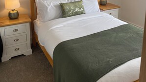 Ein Schlafzimmer mit einem Bett, zwei Nachttischen, einer Lampe auf jedem Nachttisch, einer grünen Tagesdecke und zwei gerahmten Bildern an der Wand.
