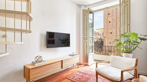 A modern living room with a wooden bench, a TV mounted on the wall, and a balcony with a view of a brick building. - Solaga - Dolores (Málaga)