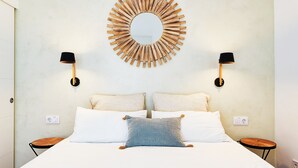 A bed with white linens, two pillows, a round mirror, and two bedside tables with lamps. - Solaga - Dolores (Málaga)