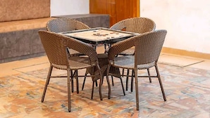 Un comedor con una mesa cuadrada y cuatro sillas de mimbre, un sofá y un suelo estampado.