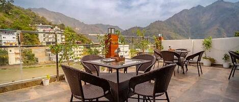 A terrace with wicker furniture and a glass table, overlooking a mountainous landscape.
