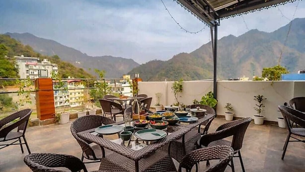 Una terraza con mobiliario de mimbre y una mesa lista para una comida, con vistas a un paisaje montañoso.